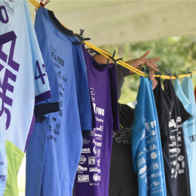 A volunteer hangs Will Bike 4 Food t-shirts on a clothesline for display.