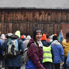 A woman with a hat for the "March for the Food Bank" turns to smile at someone behind the camera. In front of her are a crowd of other marchers.