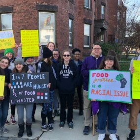 A group of students stand with representative Jim McGovern, holding signs highlighting different aspects of food insecurity.