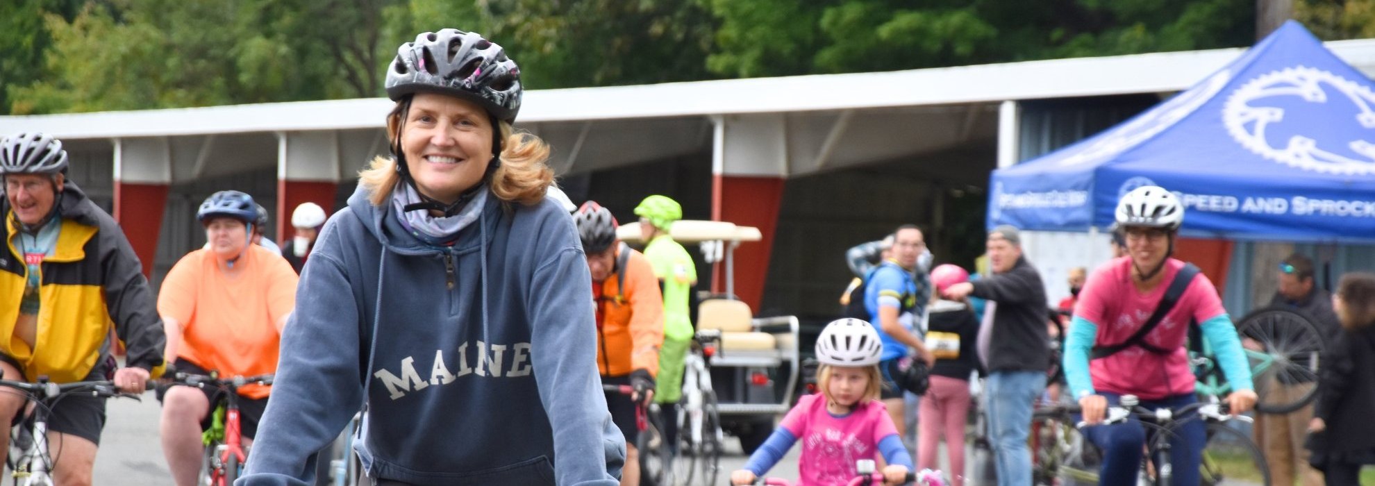 a woman on a bicycle cycles towards the camera. Others can be seen cycling in the background.